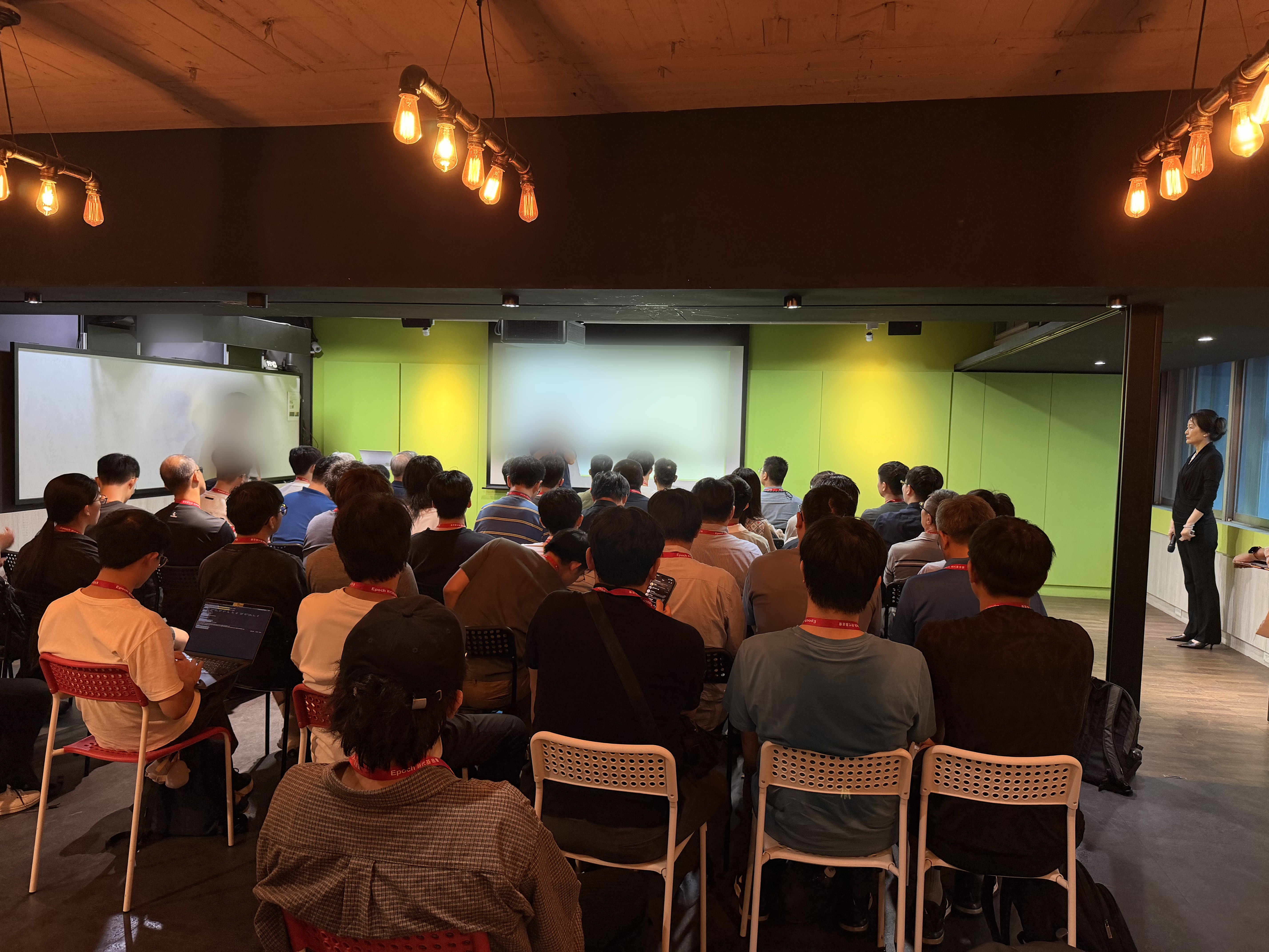 Attendees seated facing a presentation screen at a compute donation program event in Taipei; parts of the image are blurred for privacy.